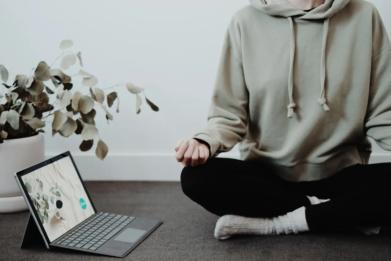 Eine Person sitzt im Schneidersitz neben einem Laptop und übt eine Entspannungsübung