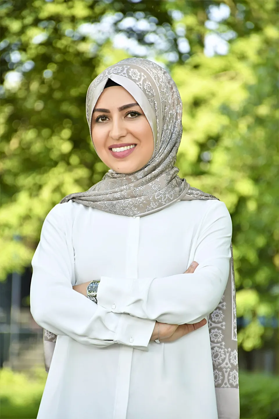 Özlem Tekdemir lächelt im Grünen, mit gemustertem Kopftuch und weißer Bluse